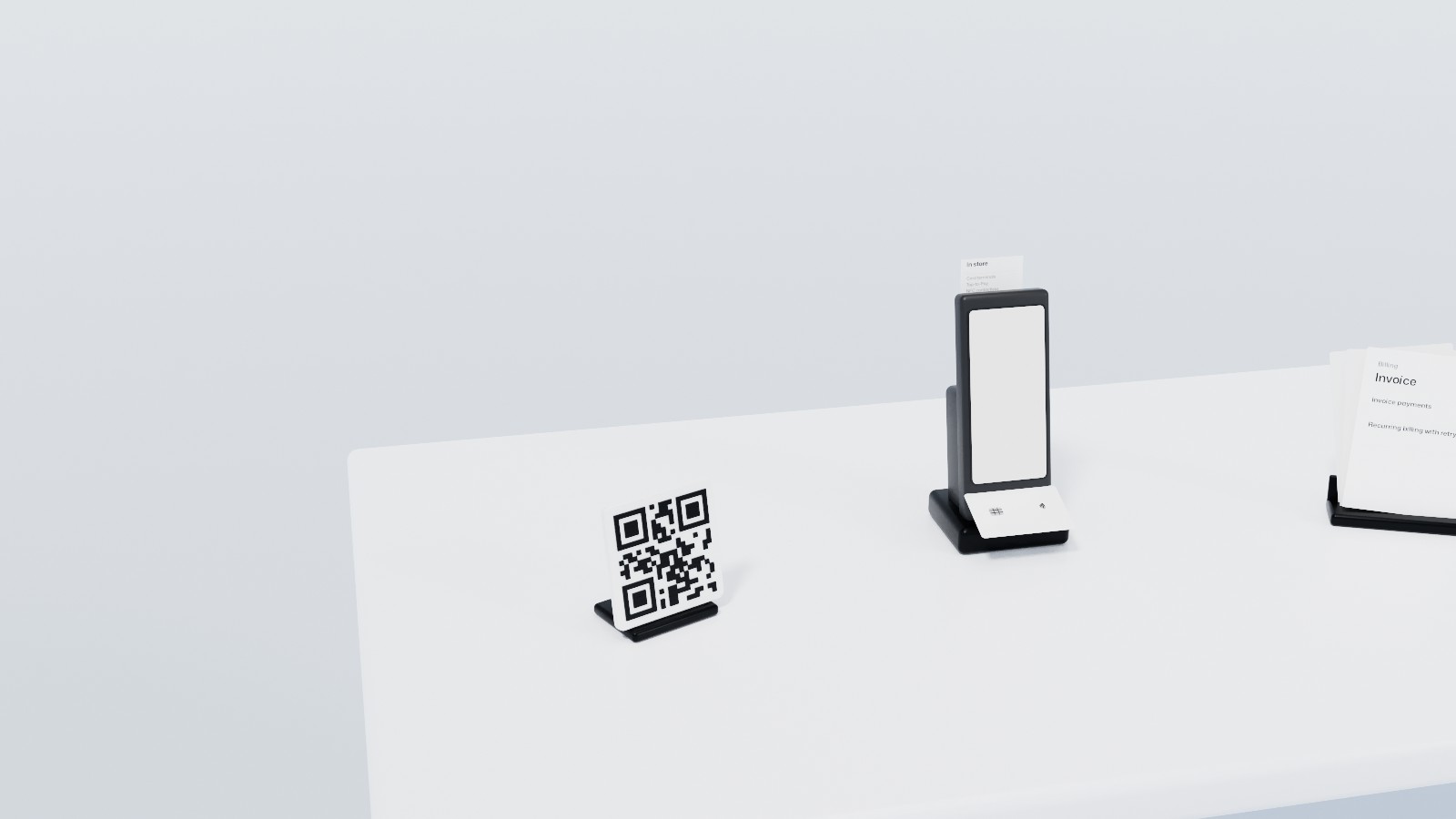 Station 02, Acceptance, close up: a handheld payment terminal in its dock with a card held over it and a slip out of its printer, a QR sign and the printed invoices of recurring billing beside it.