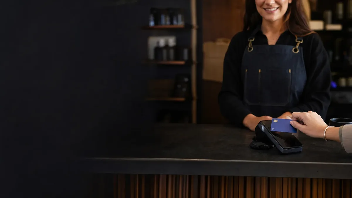 A customer taps a card on a countertop terminal at a shop counter.